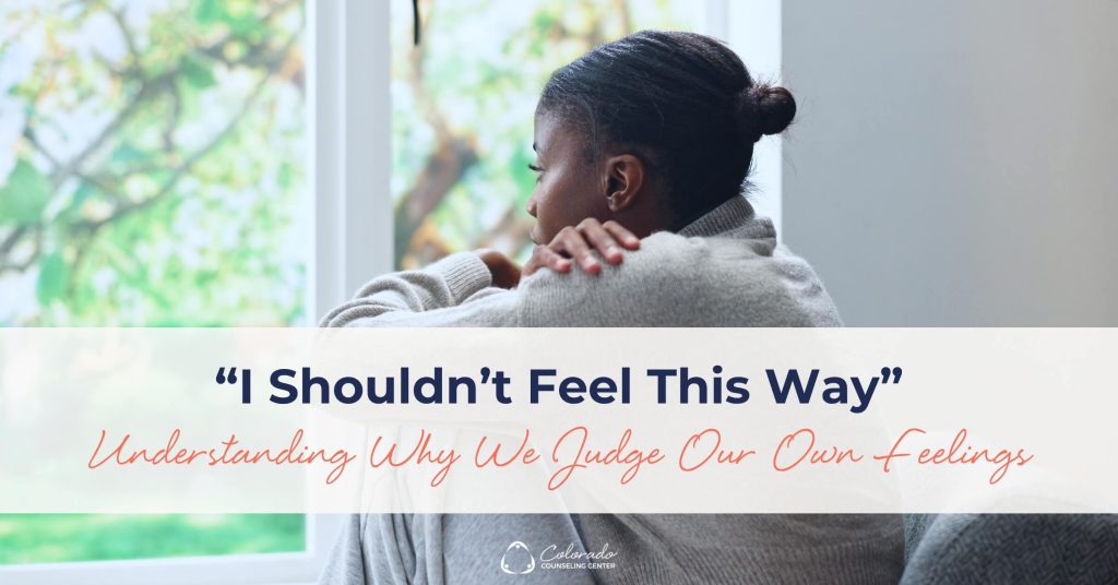 Woman resting her hand on her own shoulder, quietly processing the thought 'I shouldn't feel this way'
