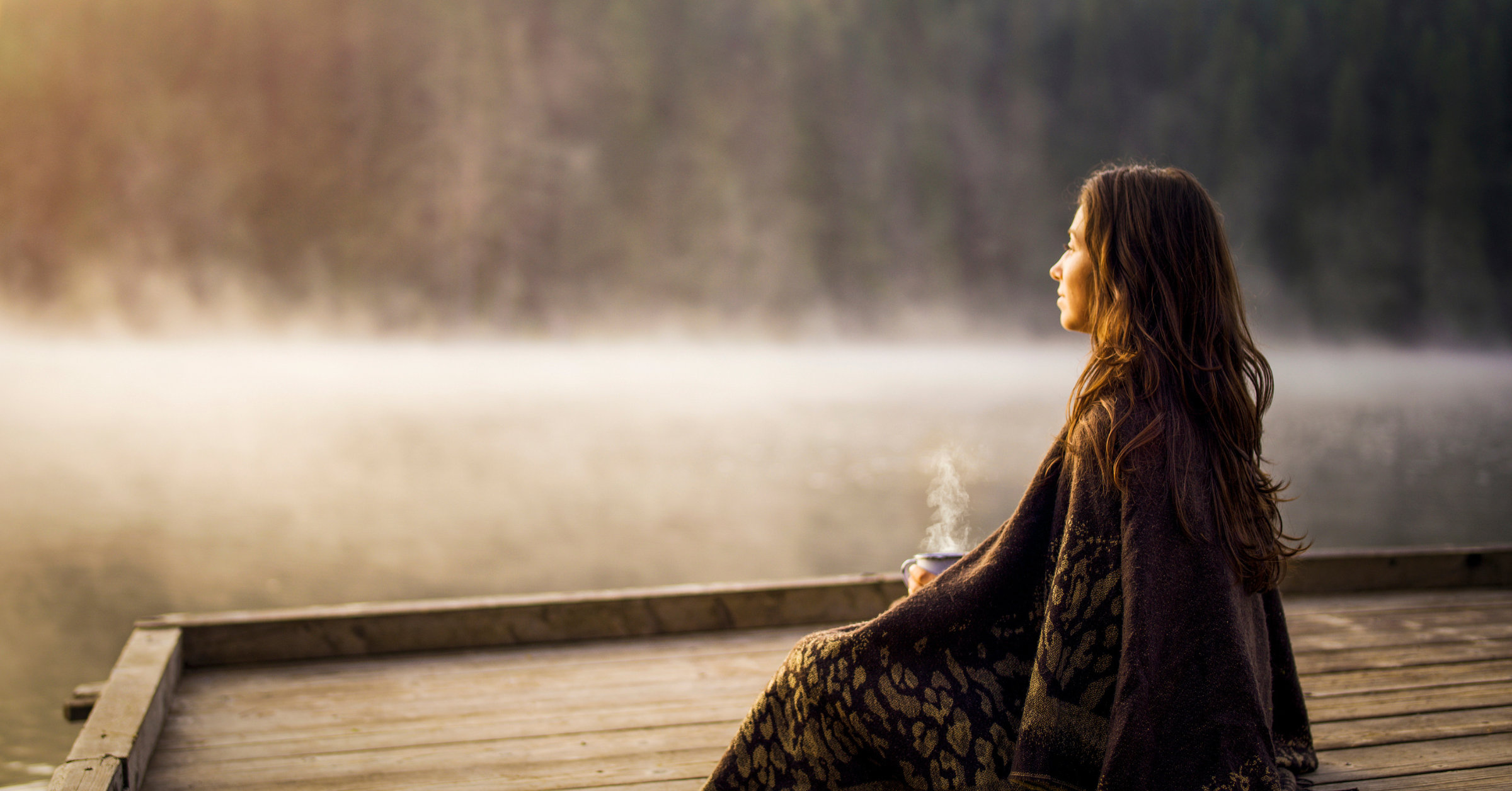 Woman sitting peacefully at sunrise by a lake, symbolizing recovery through stress and burnout therapy in Greenwood Village