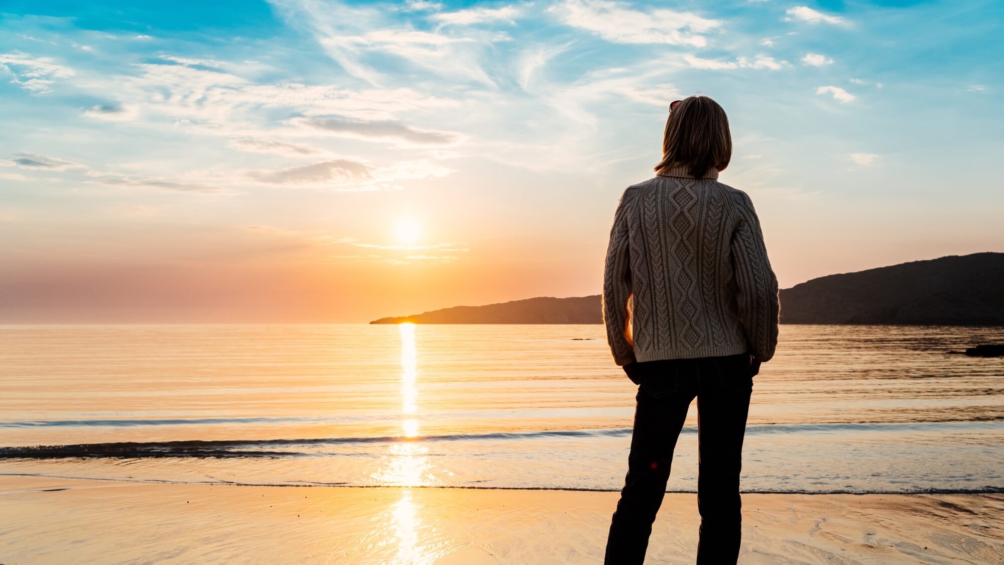 Person standing quietly on a beach at sunset, reflecting &mdash; individual counseling in Greenwood Village & Centennial.